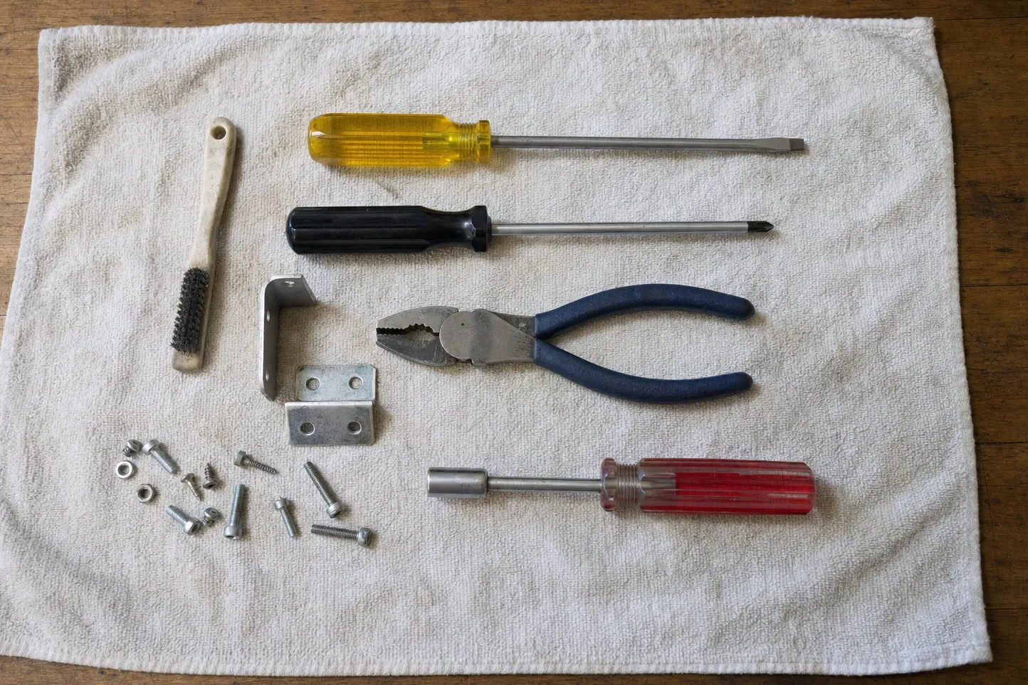 Tool cloth with a wire brush, screwdrivers, combination pliers, a nut driver, corner brackets and loose fasteners