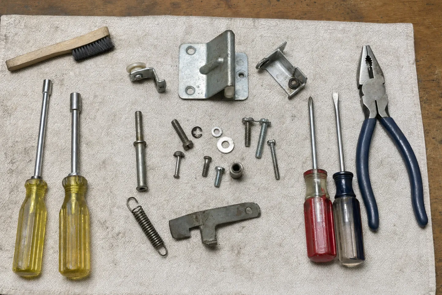 Tool cloth laid out with nut drivers, pliers, a door strike plate, a latch catch and a tension spring